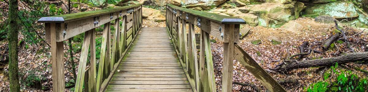 A wooden bridge with railings leading to a rocky cliff.