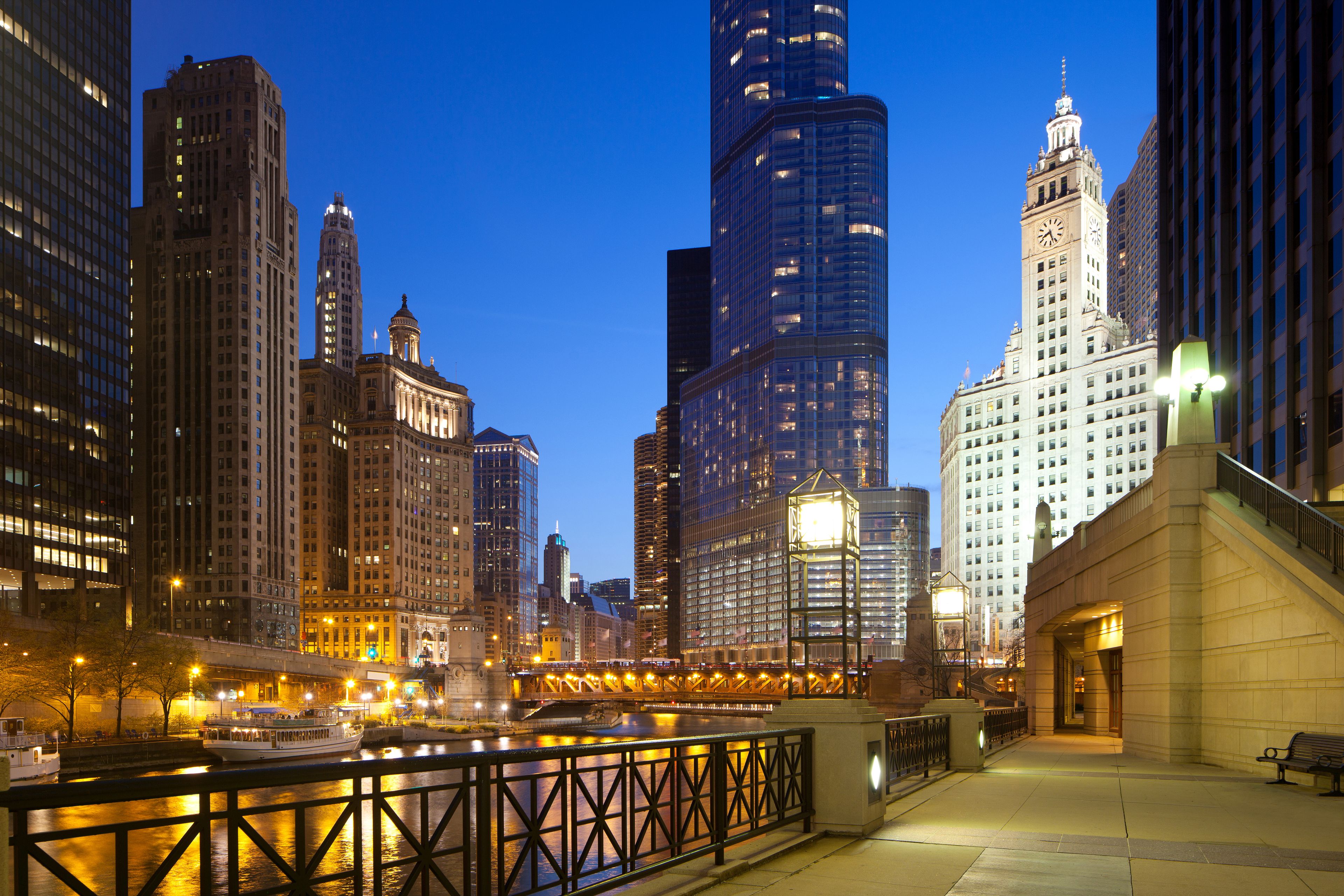 A cityscape at dusk with illuminated skyscrapers and a river.