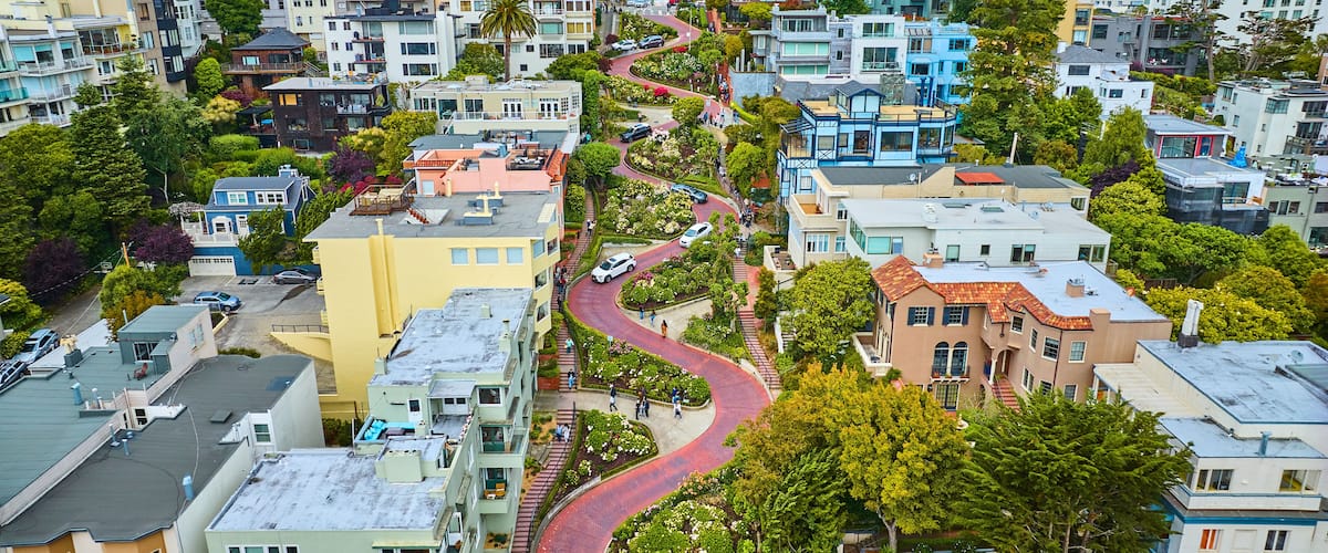 A winding street in a densely built urban area with colorful houses and lush greenery.