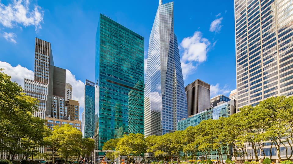 A cityscape with modern skyscrapers, a park with green grass and trees, and a clear blue sky.