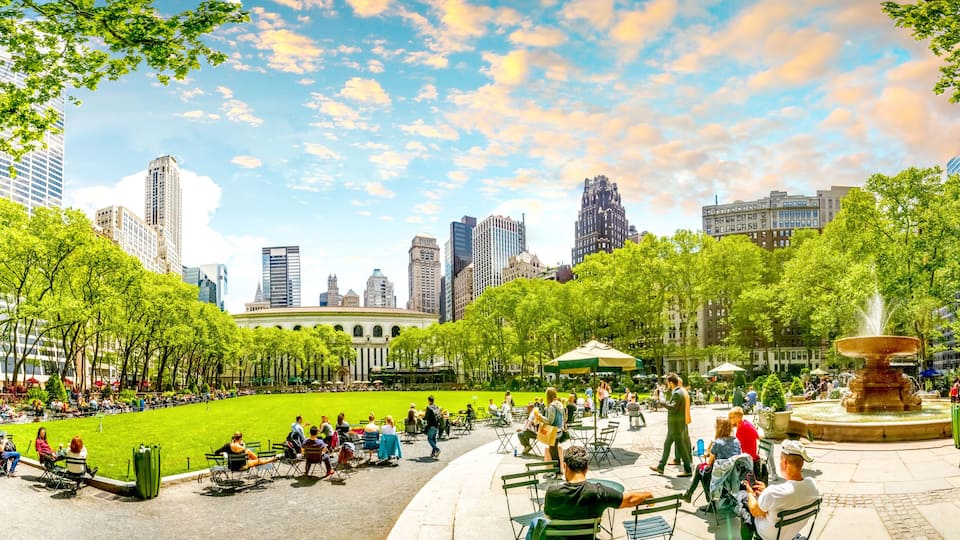 A city park with a fountain, green lawns, and tall buildings in the background.