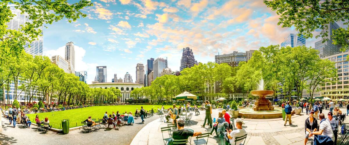 A city park with a fountain, green lawns, and tall buildings in the background.