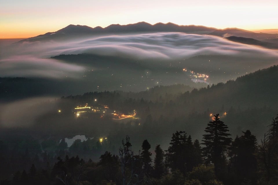 A mountain range at sunset with a village nestled in the valley below.