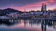 Una cittadina sul lungofiume al crepuscolo, con edifici imbiancati dalla neve e un fiume tranquillo che riflette il cielo.