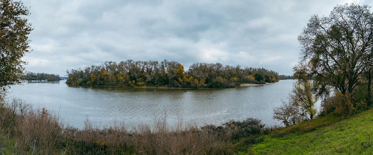 panorama captures the serene Sacramento River winding past banks lined with autumn trees