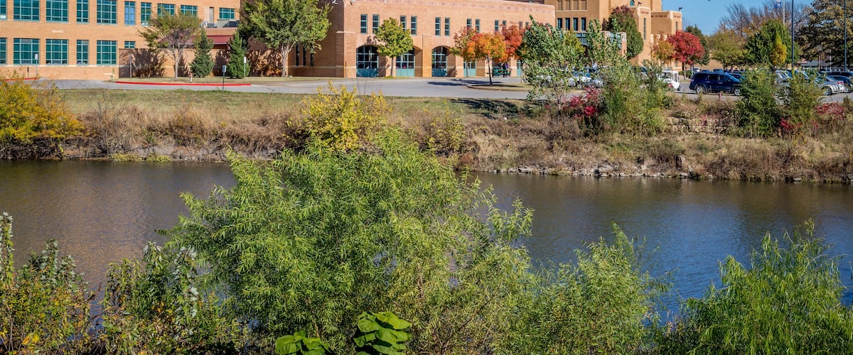 A large building with a tower, surrounded by trees and a body of water.