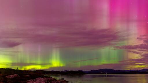 Multicoloured northern light with reflections on land and sea