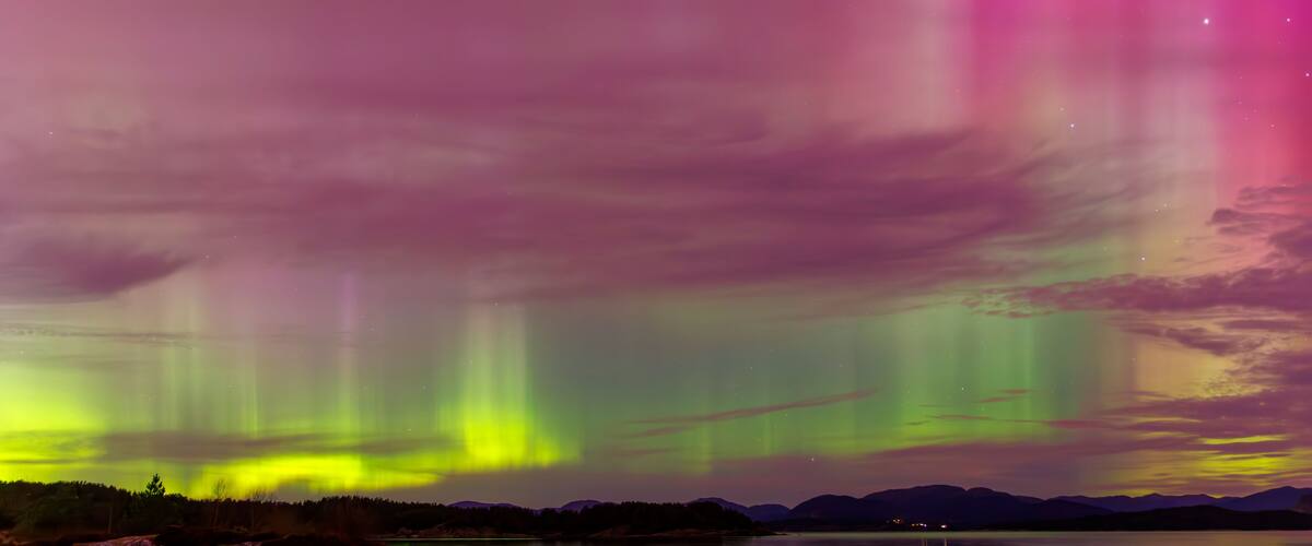 The Northern Lights over a calm lake with mountains in the background.