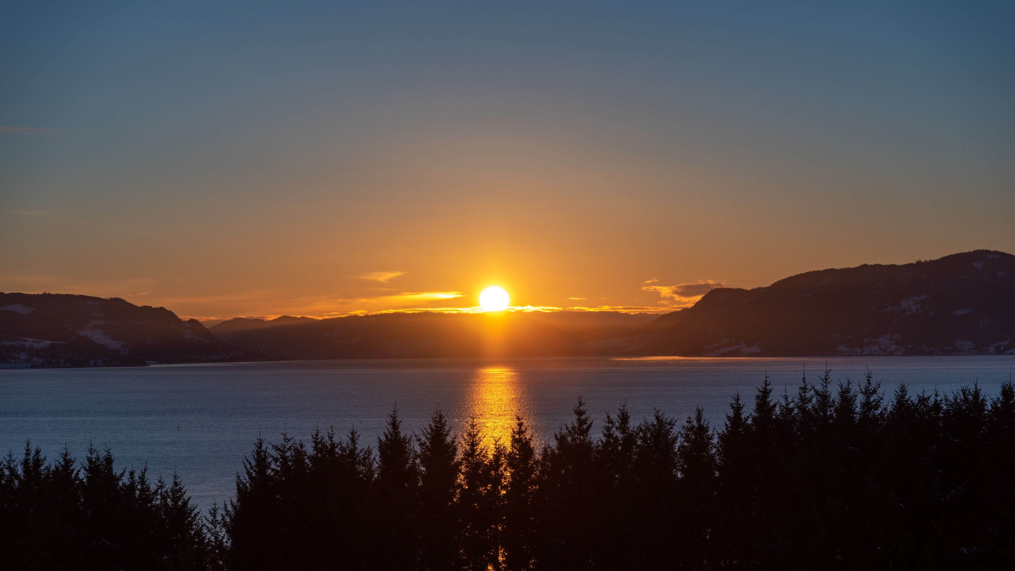 A sunset over a calm lake with mountains in the background.