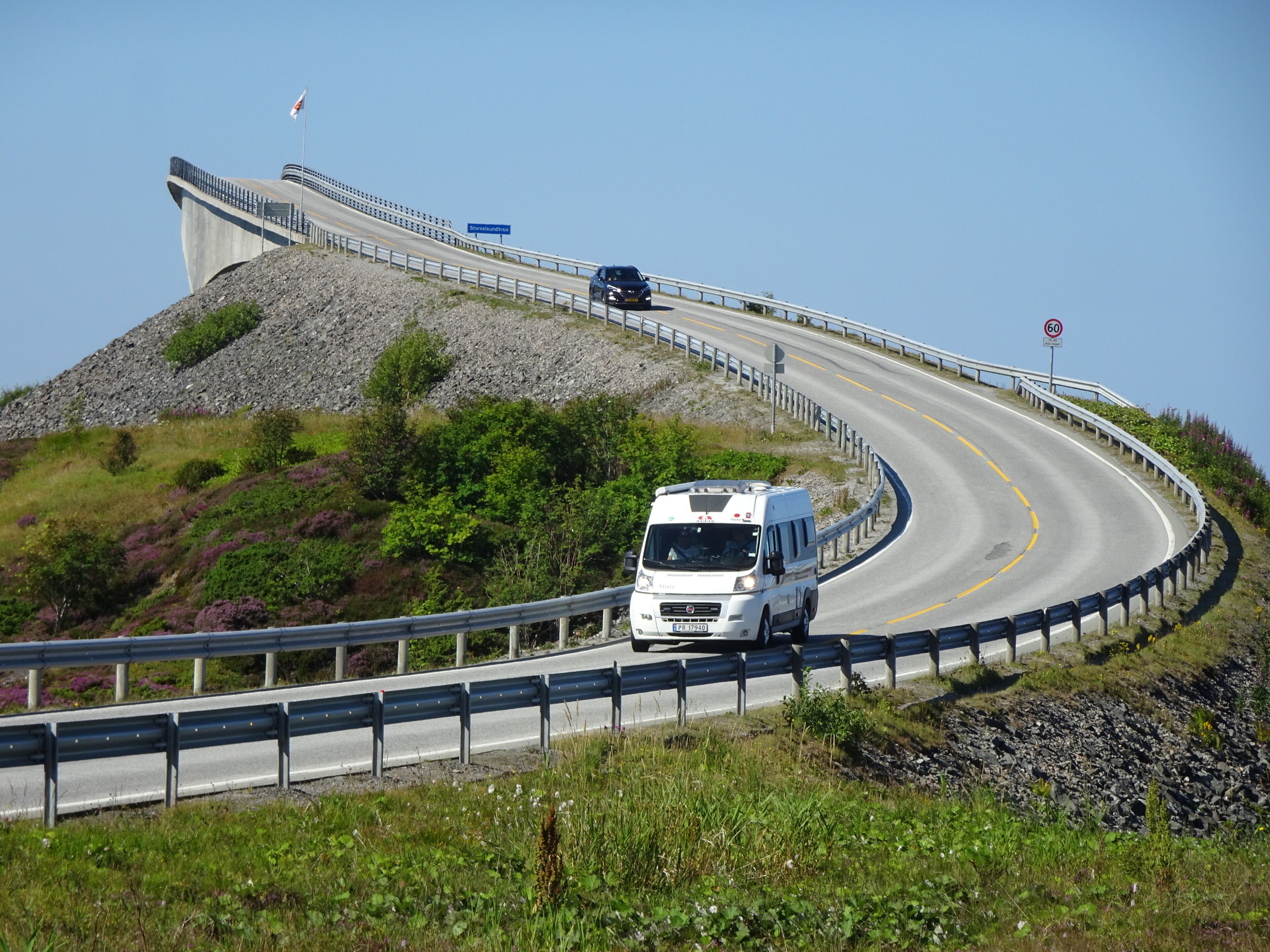 A winding road with a white van, guardrails, and a rocky hillside.