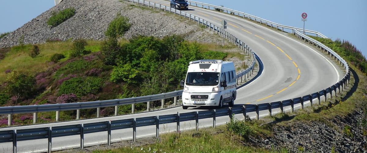 A winding road with a white van, guardrails, and a rocky hillside.