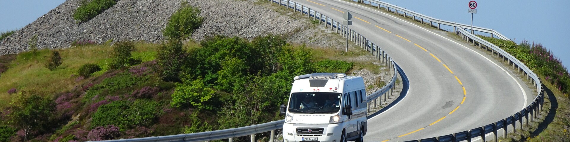 A winding road with a white van, guardrails, and a rocky hillside.