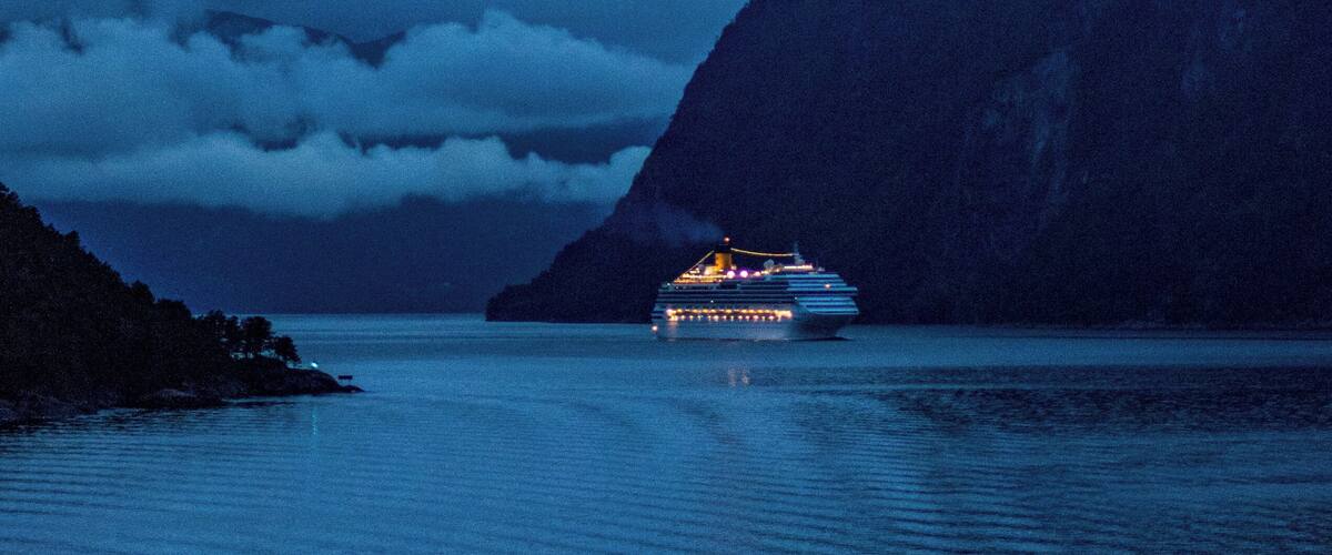 A cruise ship in a fjord with mountains in the background.