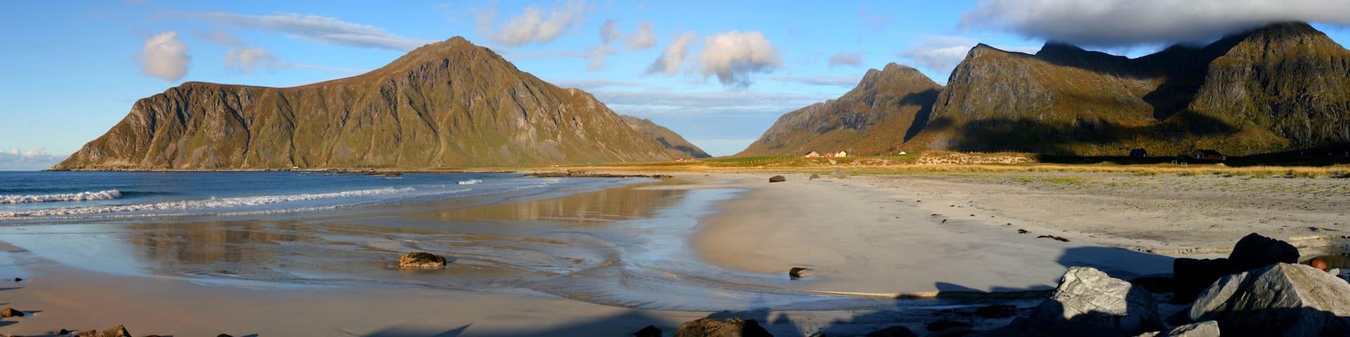 A beach with rocky outcrops and mountains in the background.