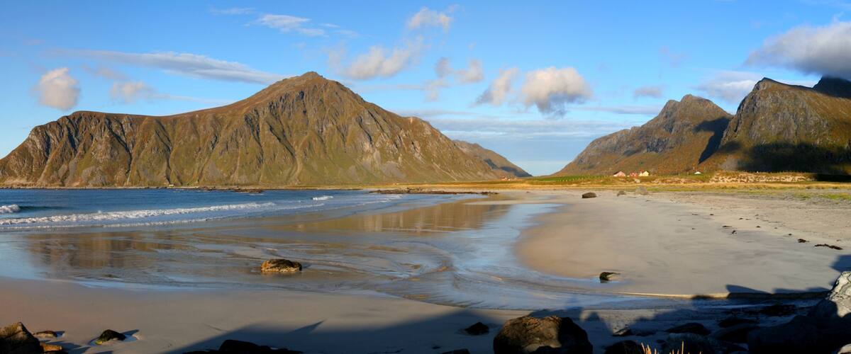 A beach with rocky outcrops and mountains in the background.