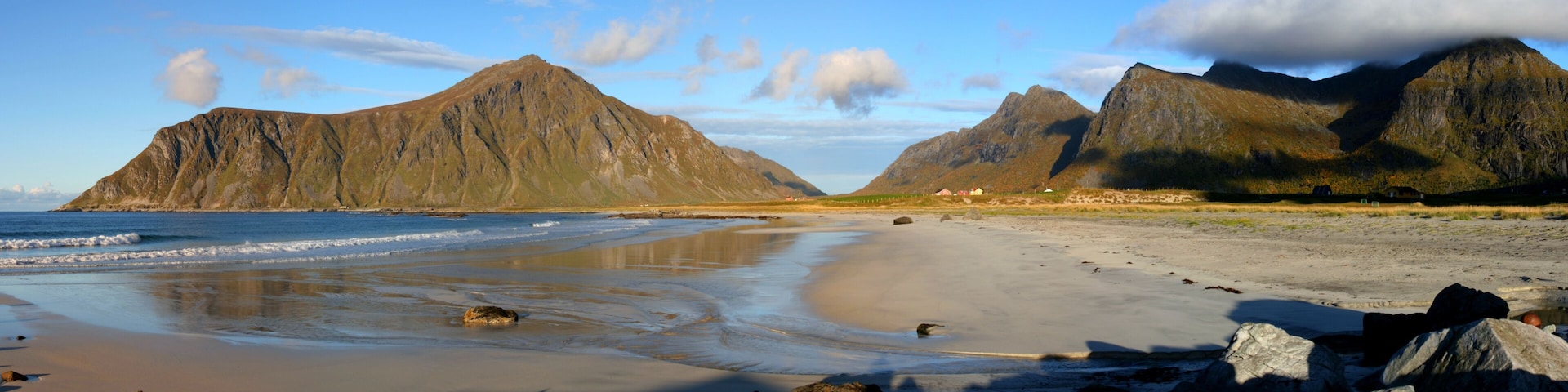 A beach with rocky outcrops and mountains in the background.