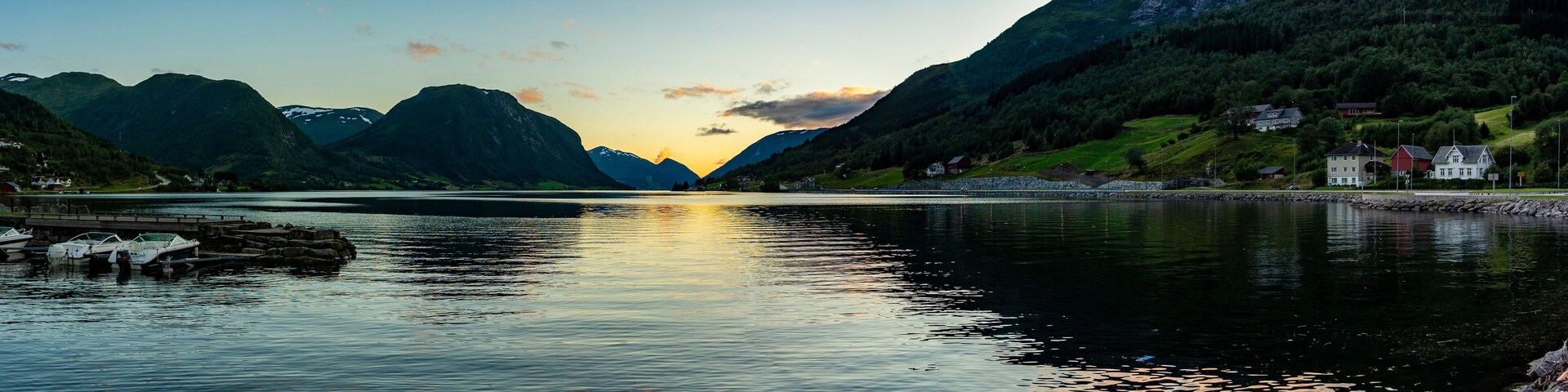 A calm lake with boats, surrounded by mountains and houses.
