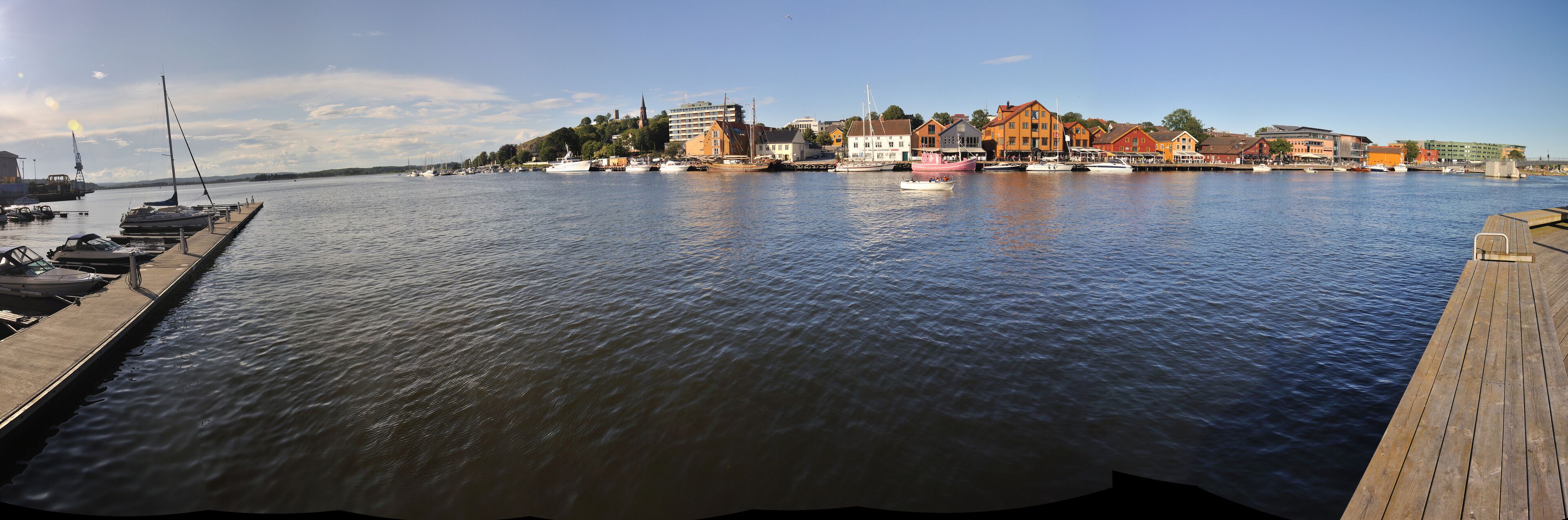 A calm harbor with boats docked, a wooden pier, and colorful buildings along the waterfront.