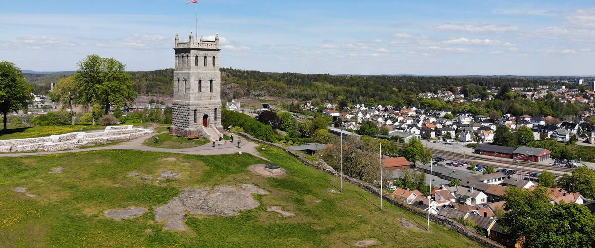 Created by dji drone camera of Slottsfjell an architecture building from medieval times in the oldest city of Norway with a village in the background and the Norwegian flag on top in the summer