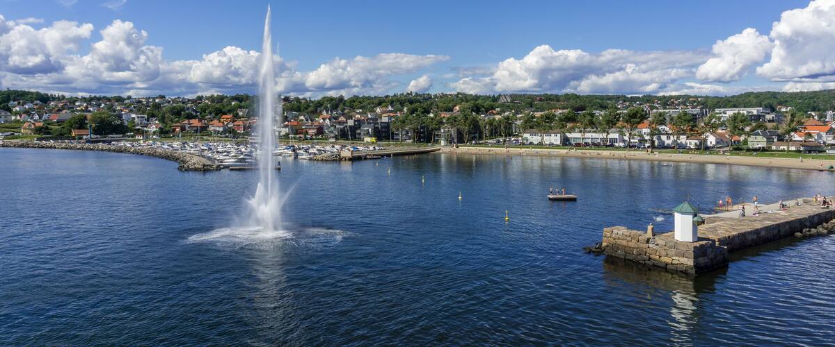 A coastal town with a prominent water fountain, marina, and a stone pier.