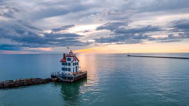 Un faro en un muelle con el atardecer de fondo.