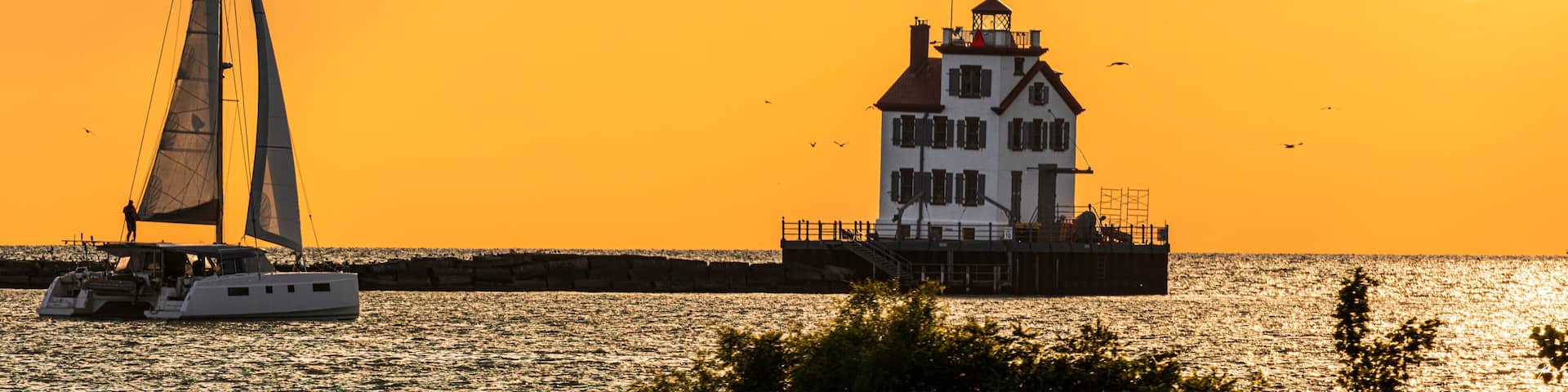 Sailboat approaches the Lorain Harbor Lighthouse on Lake Erie in the Great Lakes, at sunset.