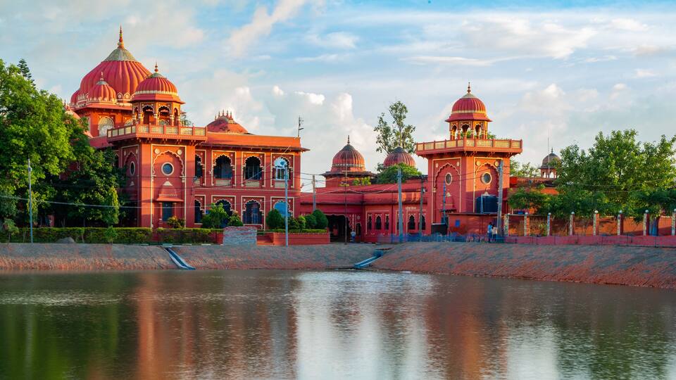 A large, ornate building with multiple domes and arches, situated beside a calm body of water.