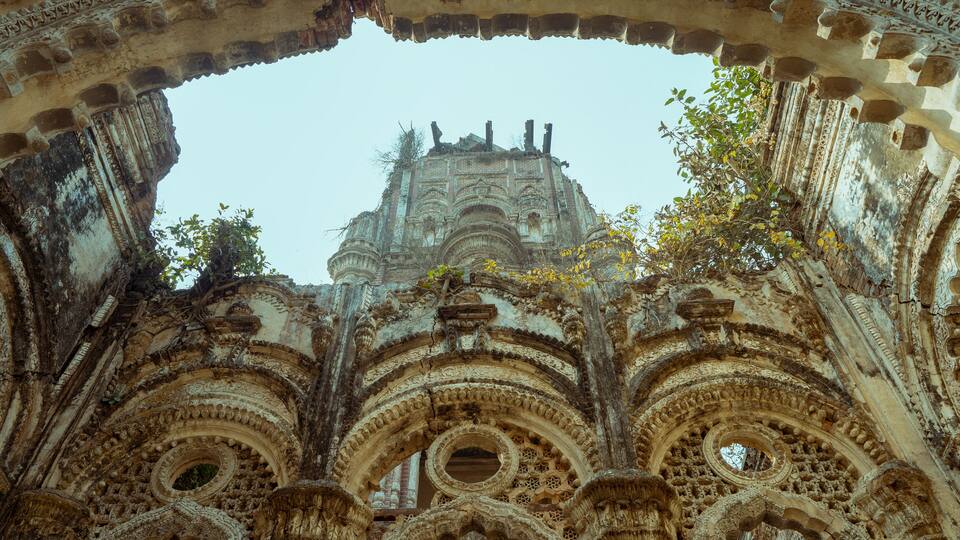 An ornate Gothic archway with intricate carvings and a view of a historic building in the background.