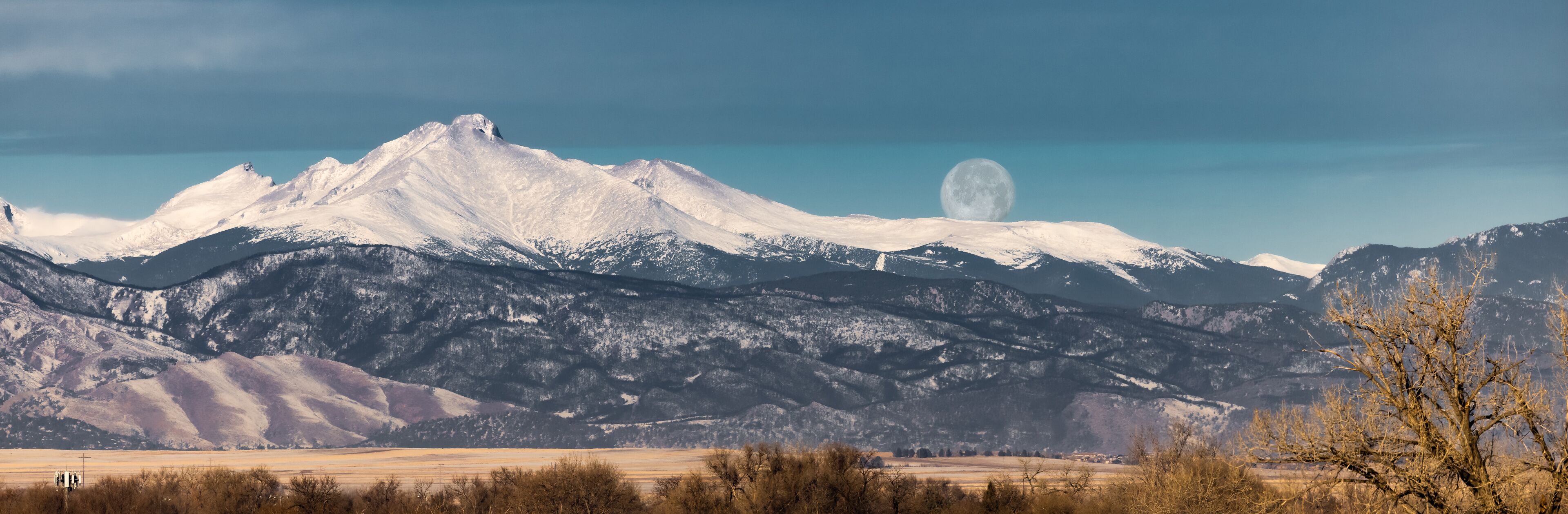 A snow-capped mountain range with a visible moon in the sky.