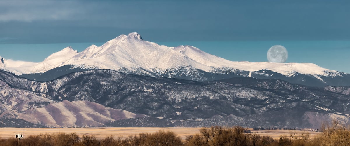 A snow-capped mountain range with a visible moon in the sky.