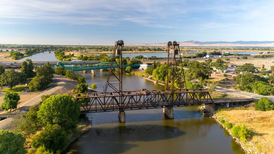 A steel bridge over a river with a highway passing underneath.