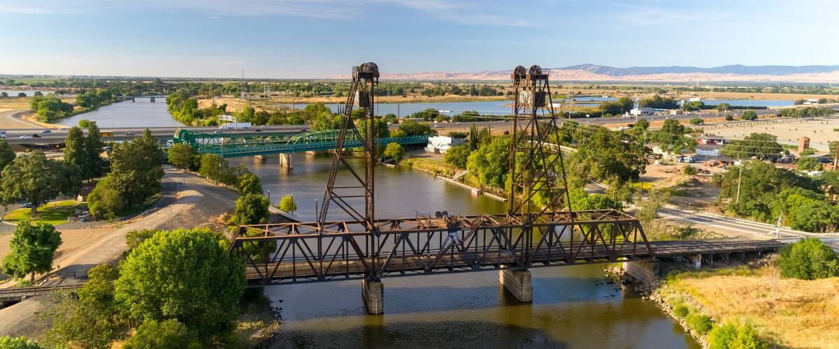 A steel bridge over a river with a highway passing underneath.