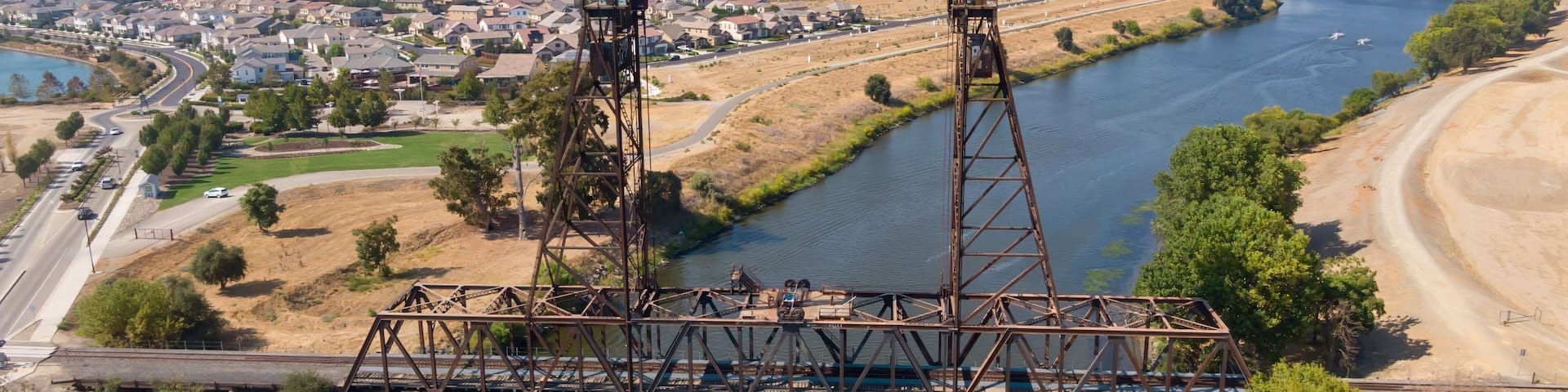 Aerial view of the Mossdale Railroad Bridge, a historic vertical-lift bridge, spanning the San Joaquin River in Lathrop, California, USA, Residential areas in the background.
