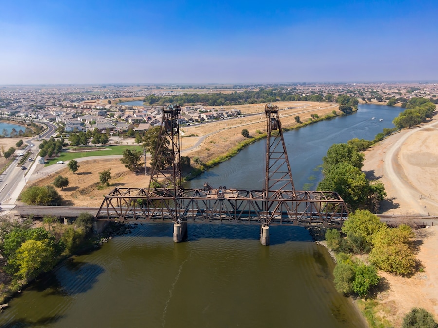 Aerial view of the Mossdale Railroad Bridge, a historic vertical-lift bridge, spanning the San Joaquin River in Lathrop, California, USA, Residential areas in the background.
