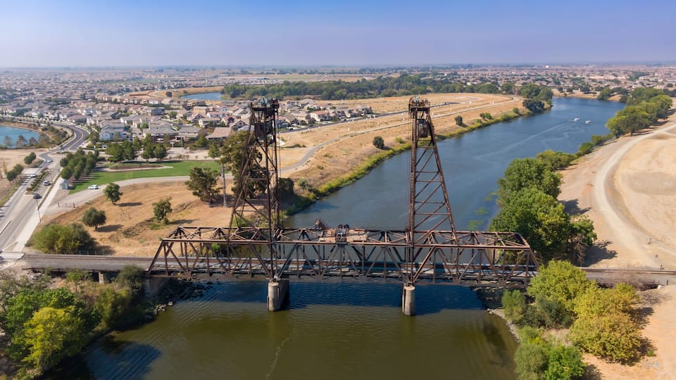 A large metal bridge spanning a river with a town in the background.