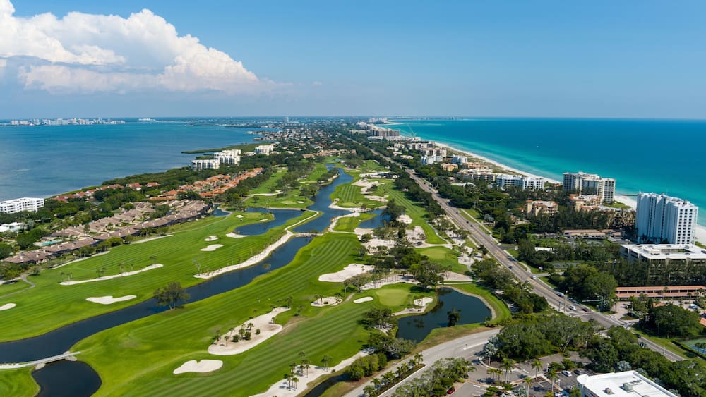 A coastal cityscape with a golf course, residential areas, and a marina.