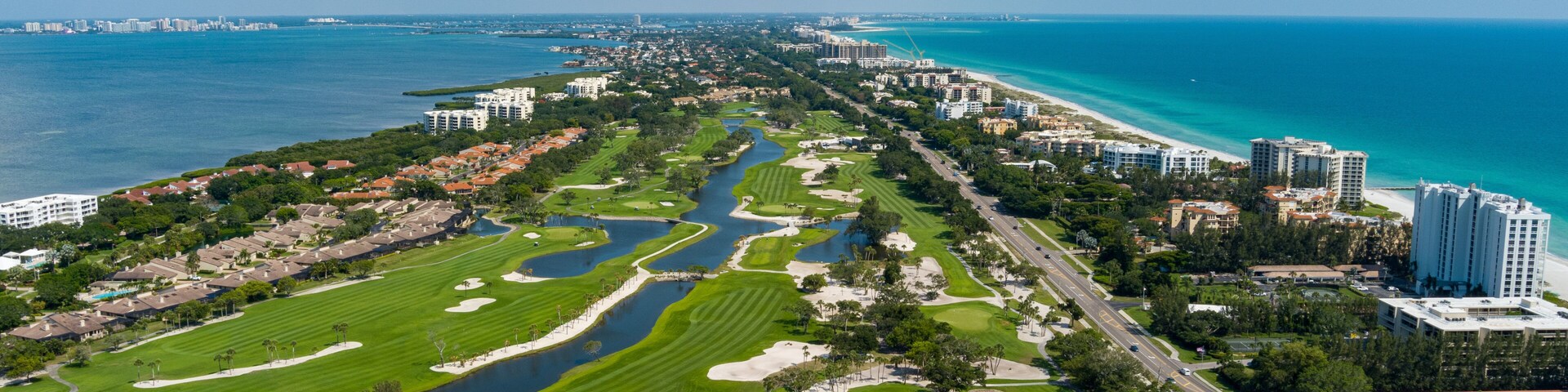 Een kuststadsgezicht met een golfbaan, woonwijken en een jachthaven.