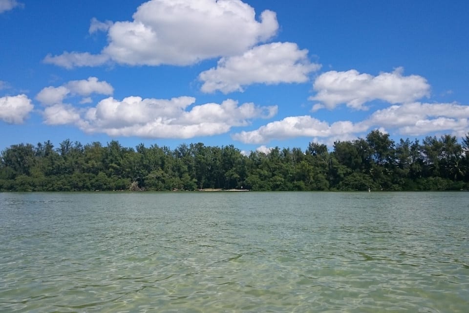 Un lac aux eaux limpides, entouré d’une végétation luxuriante et verdoyante, sous un ciel partiellement nuageux.