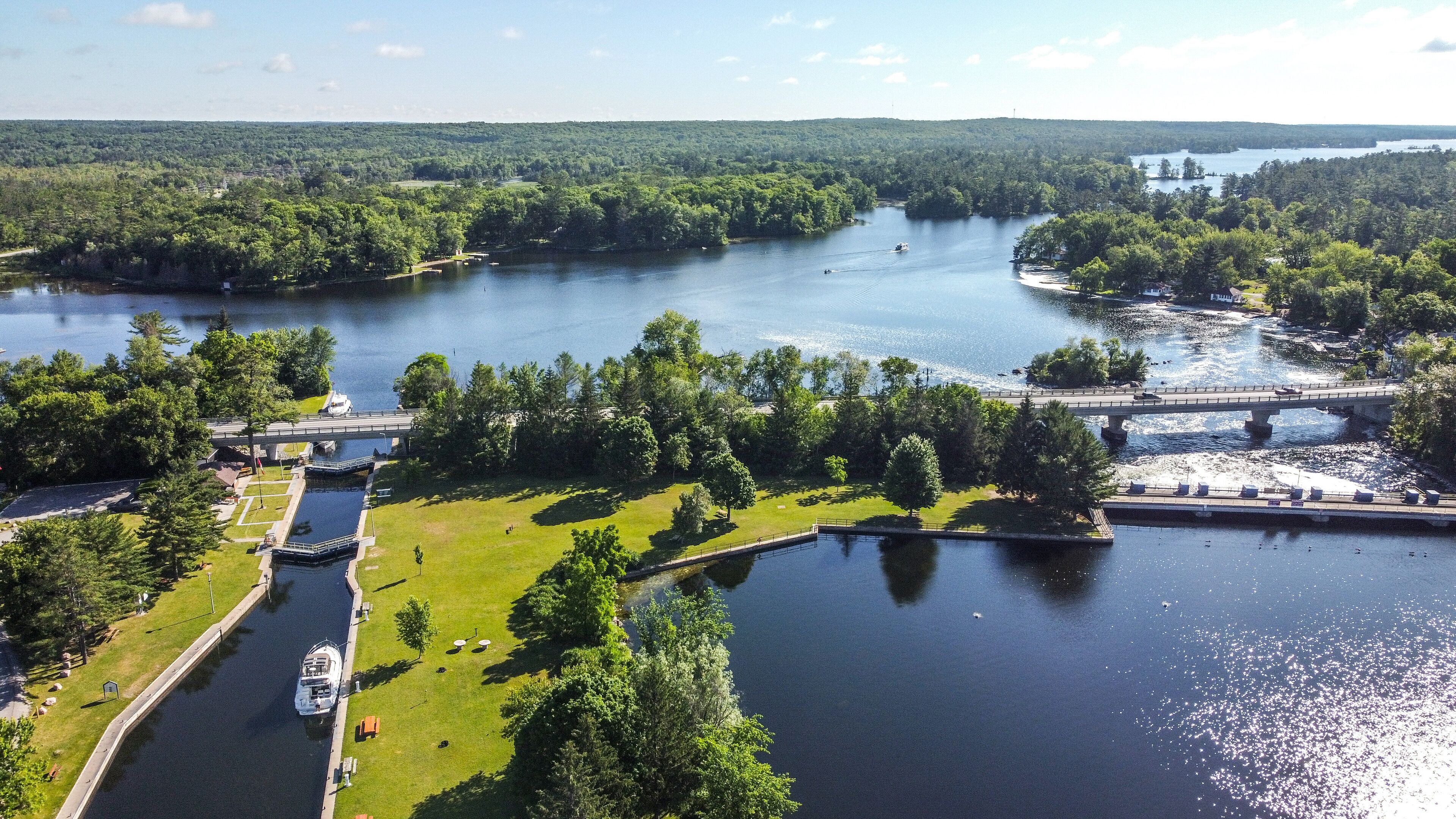 A river with a bridge, boats, and a grassy area with trees.