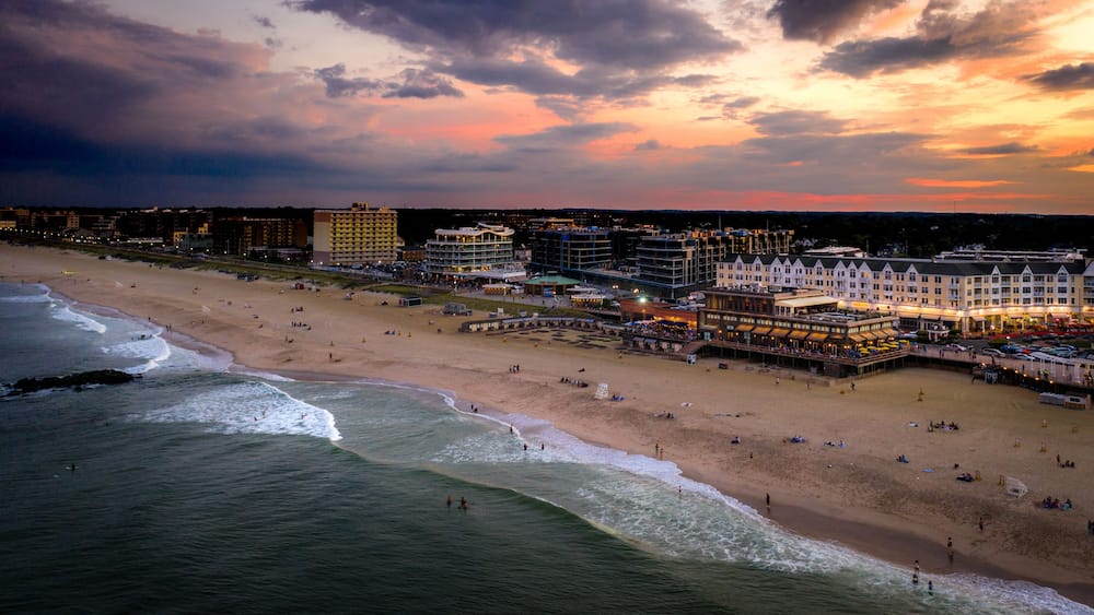 Un paysage urbain côtier avec une plage, des vagues de l’océan et divers bâtiments, notamment des hôtels et des restaurants.