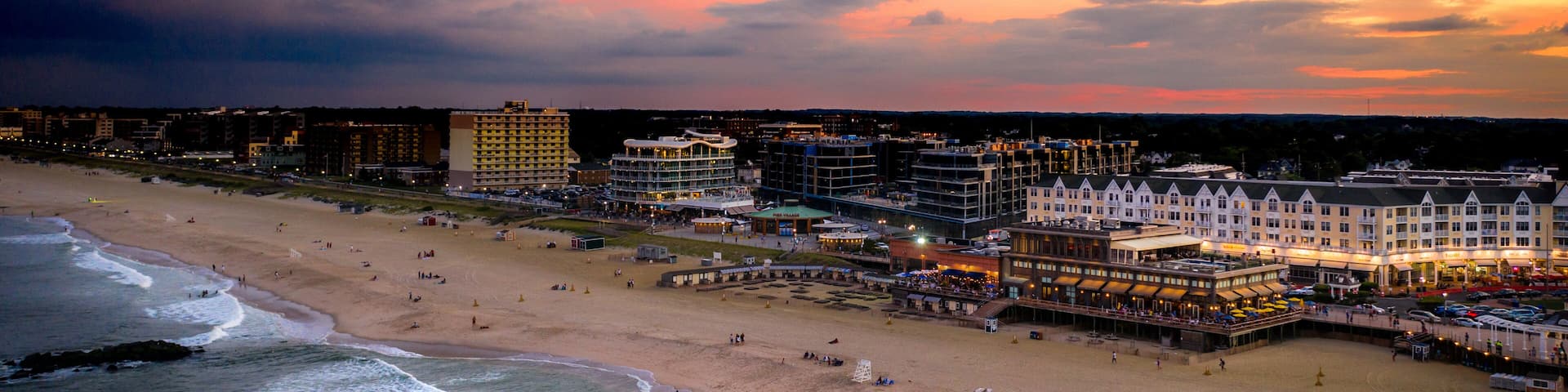 A coastal cityscape with a beach, ocean waves, and a variety of buildings including hotels and restaurants.