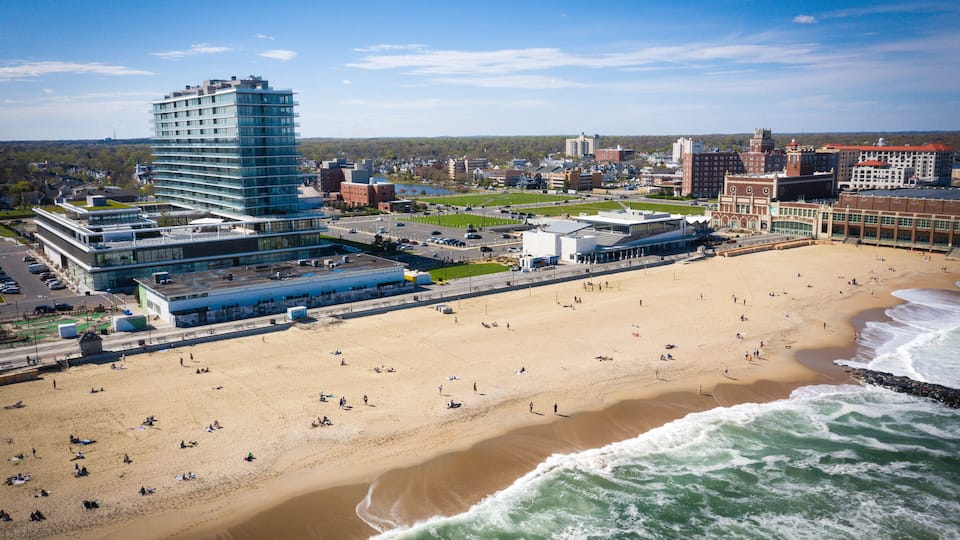 A coastal cityscape with a sandy beach, a large hotel, and various buildings.