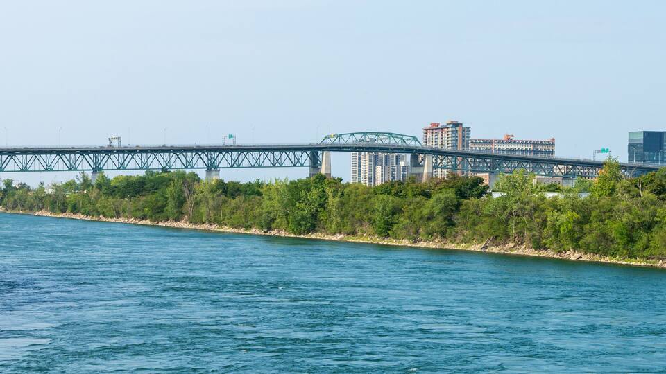 A river with a bridge, trees, and buildings in the background.