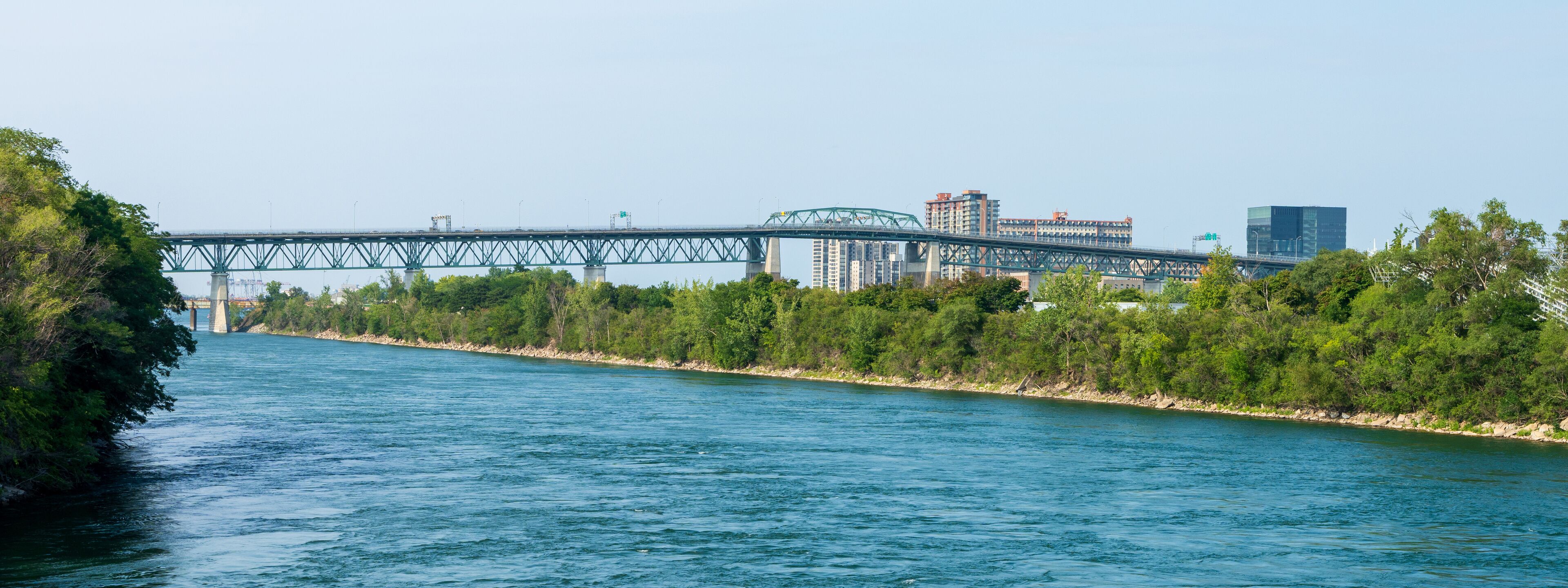 A river with a bridge, trees, and buildings in the background.