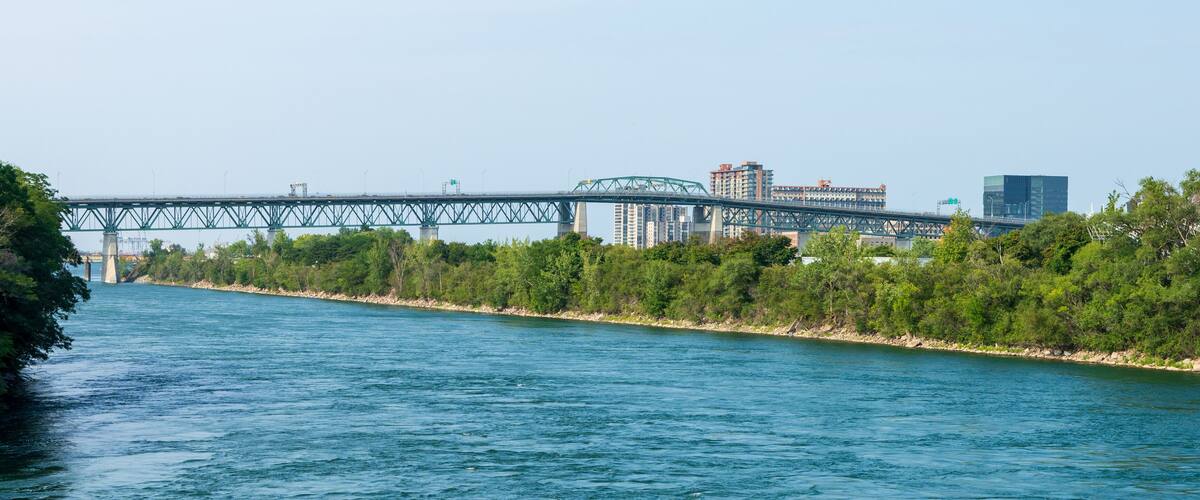 A river with a bridge, trees, and buildings in the background.