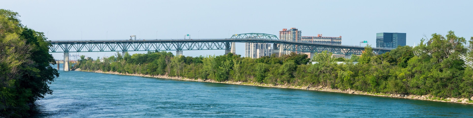 A river with a bridge, trees, and buildings in the background.