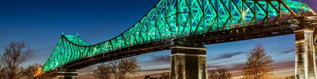A large bridge with green lighting, spanning over a body of water with city buildings in the background.