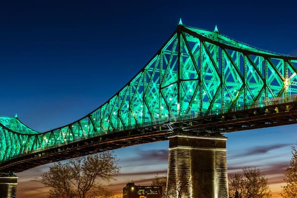Un grand pont illuminĂ© de lumiĂšres vertes, qui enjambe une Ă©tendue dâeau, avec des bĂątiments de la ville en arriĂšre-plan.