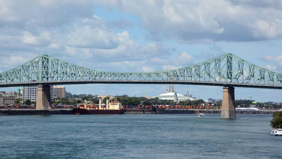 A large green bridge spanning a river with a cityscape in the background.