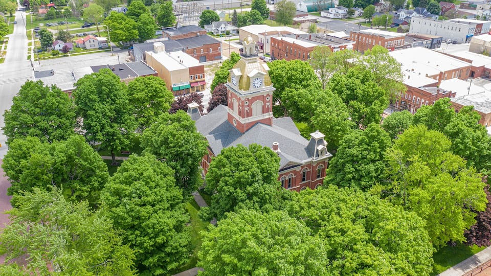 A historic town center with a prominent clock tower surrounded by lush green trees and red brick buildings.